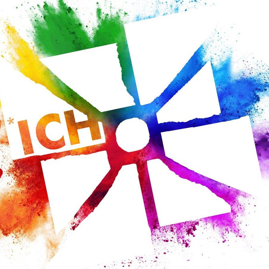 Das Bild zeigt ein stilisiertes Windrad, dessen Flügel in den Farben des Regenbogens (Rot, Orange, Gelb, Grün, Blau, Lila) gefärbt sind und von farbigen Spritzern umgeben werden. In einem der Flügel steht das Wort "ICH" in orangefarbener Schrift. Das Windrad hat einen weißen Hintergrund und die Farben verlaufen leicht in den Hintergrund hinein, was den Eindruck von Farbspritzern oder -wolken erweckt.